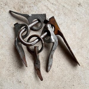May include: A collection of four weathered metal pitons with integrated rings, featuring visible signs of oxidation and rust. Each piece is stamped with the text R. CASSIN, showcasing a pointed blade design intended for insertion into rock crevices.