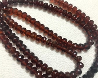 May include: A strand of dark red faceted gemstone beads. The beads are round and have a smooth, polished finish.