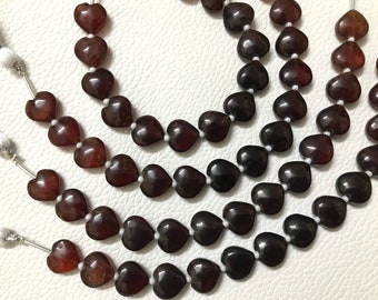 May include: A strand of dark brown heart-shaped gemstone beads. The beads are strung on a silver wire and are arranged in a circular pattern.