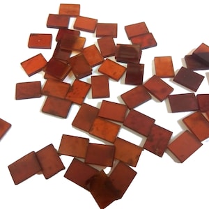 May include: A collection of small, rectangular, translucent, amber-colored glass tiles. The tiles are scattered on a white surface.