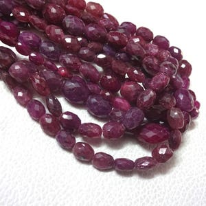 May include: A strand of deep red ruby gemstone beads, each bead is faceted and oval shaped. The beads are strung together to create a necklace or bracelet.