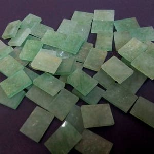 Könnte beinhalten: Eine Sammlung kleiner, rechteckiger, grüner Glasfliesen mit mattem Finish. Die Fliesen sind in einem zufälligen Muster angeordnet.