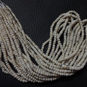 May include: A strand of white gemstone beads. The beads are small and round, and they have a slightly rough texture. The beads are strung on a white thread.