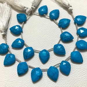 May include: A strand of turquoise gemstone beads with a faceted teardrop shape. The beads are strung on silver wire and have a dark blue color with black veins.