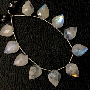 May include: A strand of iridescent moonstone beads, each bead is a pear-shaped gemstone with a faceted cut. The beads are strung on a silver wire.