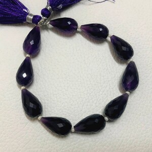 May include: A strand of faceted amethyst teardrop beads, ranging in color from deep purple to lighter shades. The beads are strung together with small white spacers. A purple tassel is visible at the top.