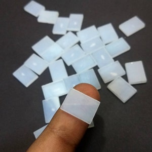 May include: A pile of white, rectangular, translucent stones. The stones are smooth and have a slightly cloudy appearance. One stone is being held by a finger.