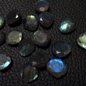 May include: A collection of 14 iridescent labradorite gemstones, each with a unique, faceted shape. The stones are a mix of dark blue, green, and grey hues, with a shimmering, metallic sheen.