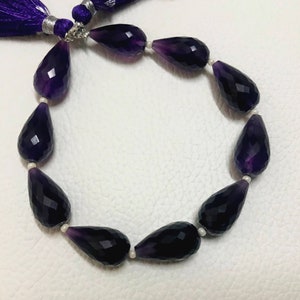 May include: A strand of faceted, teardrop-shaped amethyst beads. The deep purple beads are strung together with small white beads. A purple tassel is visible at the top of the image.