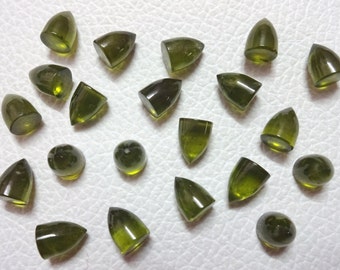 Puede incluir: Una colección de 20 cabujones de piedras preciosas verdes en varias formas, incluyendo redondas y puntiagudas, con un acabado pulido.