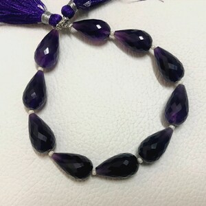 May include: A strand of faceted, teardrop-shaped amethyst beads. The beads are a deep purple color and are strung together with small white beads. A purple tassel is attached to the end of the strand.