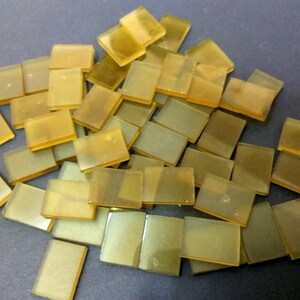 May include: A pile of small, translucent, amber-colored glass tiles. The tiles are rectangular and have a smooth, polished surface.