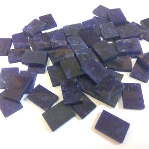 May include: A pile of small, square, purple and blue mosaic tiles. The tiles are made of natural stone and have a rough, textured surface.