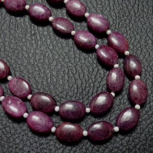 May include: A double strand necklace made of oval-shaped, dark purple gemstones with white beads between each gemstone.
