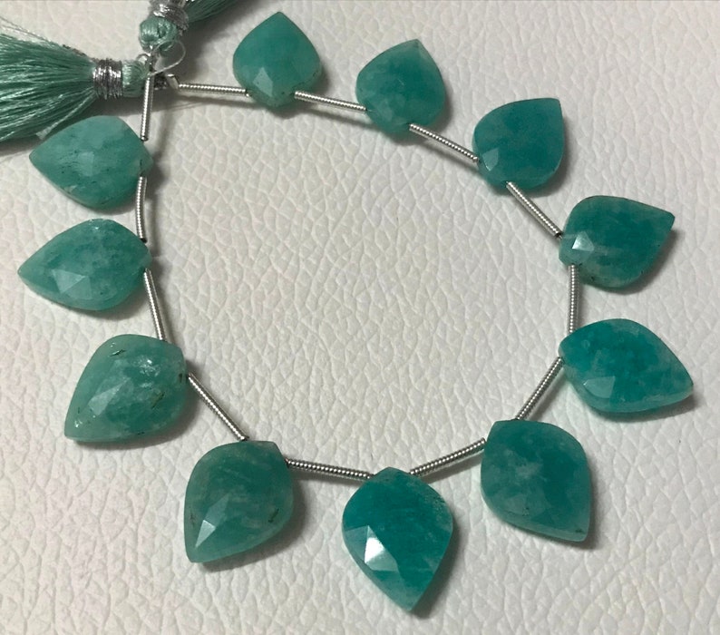 May include: Strand of faceted, teal-colored gemstone beads. Each bead is leaf-shaped and strung on a silver-colored wire. A matching teal tassel is visible at the top. The beads have a polished, translucent appearance.