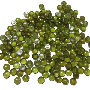 以下が含まれることがあります： 丸い緑色のガラスビーズがたくさんあります。ビーズは滑らかで光沢があり、白い背景に散らばっています。