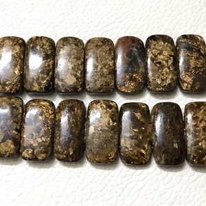 May include: A strand of brown and gold rectangular gemstone beads. The beads have a speckled, marbled appearance.