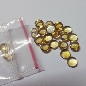 Puede incluir: Primer plano de una pequeña bolsa de plástico llena de una gran cantidad de cuentas de vidrio redondas, translúcidas, de color amarillo ámbar.