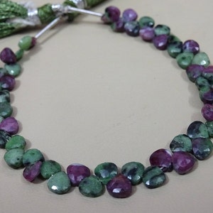 May include: A strand of green and pink gemstone beads in a heart shape. The beads are strung on a silver thread.