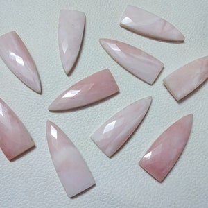 May include: Twelve pink opal cabochons in a pointed shape. The stones are translucent and have a light pink color.