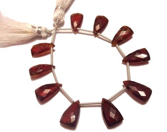 May include: A strand of 10 faceted, teardrop-shaped, reddish-brown gemstone beads strung on a silver wire.