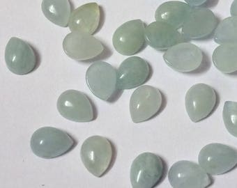 May include: A collection of aquamarine teardrop-shaped gemstones. The stones are a pale blue-green color and have a smooth, polished surface. They are scattered across a white surface, showcasing their individual shapes and subtle variations.