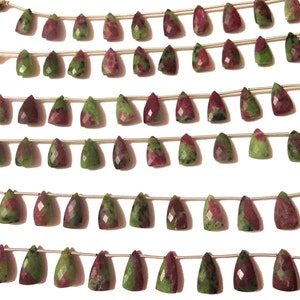 May include: A strand of green and pink gemstone beads, each bead is faceted and shaped like a teardrop. The beads are strung on a silver cord and have tassels on each end.