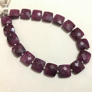Peut inclure: Un collier de perles de pierres précieuses violettes, chaque perle est facetée et de forme carrée. Les perles sont enfilées sur un cordon blanc avec des glands à l'extrémité.