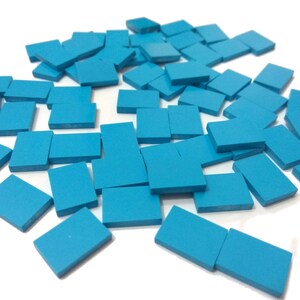 May include: A pile of small, square, turquoise blue tiles. The tiles are scattered on a white surface.