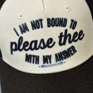 Peut inclure: Un chapeau de camionneur blanc et noir avec le texte "I am not bound to please thee with my answer - Shakespeare -" imprimé sur le devant.
