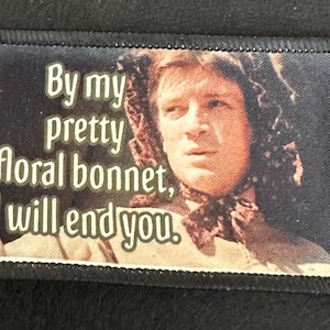May include: A black and white embroidered patch with a woman wearing a floral bonnet. The text on the patch reads "By my pretty floral bonnet, I will end you."