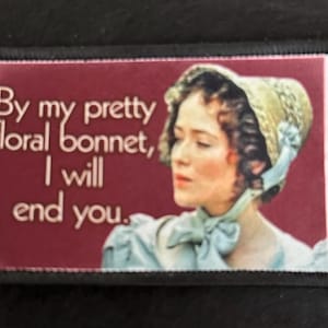 May include: A vintage-style embroidered patch with a woman wearing a floral bonnet and a blue dress. The text on the patch reads "By my pretty floral bonnet, I will end you."