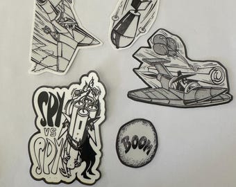 May include: Five black and white stickers with illustrations of a spy, a bomb, a plane, and the word "BOOM". The spy sticker says "SPY VS SPY".