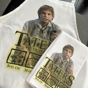 Op de afbeelding: Witte schort en bijpassende keukendoek met een afbeelding van een man met een pijp. De tekst op de schort en de doek luidt "Taters, Potatoes" met kookinstructies "Boil Em, Mash Em, Stick Em in a Stew."