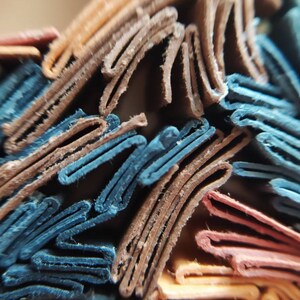 May include: Close-up of a stack of folded paper, showing the edges of the paper in various colors, including blue, brown, orange, and red.