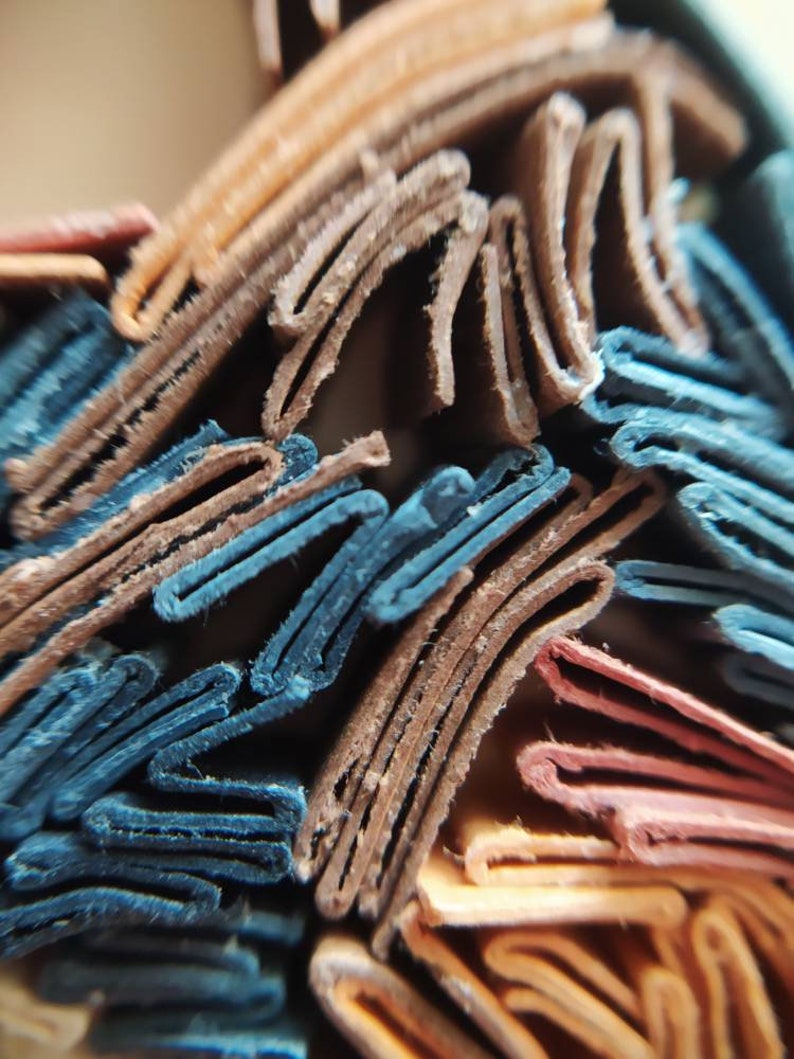 May include: Close-up of a stack of folded paper, showing the edges of the paper in various colors, including blue, brown, orange, and red.