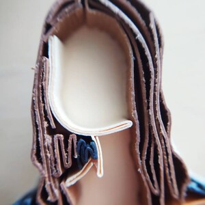 May include: A close-up of a paper craft sculpture of a person's head with brown hair. The hair is made of many layers of paper, creating a textured look.