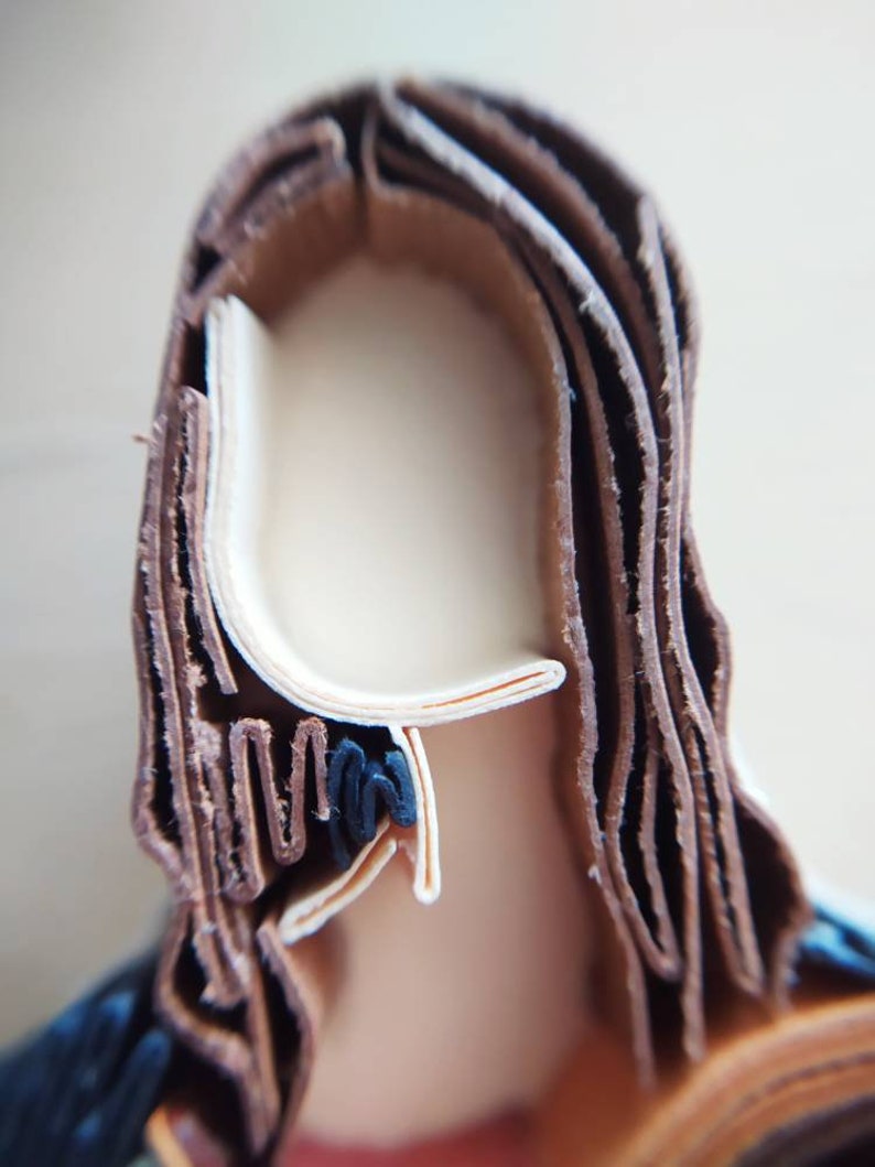 May include: A close-up of a paper craft sculpture of a person's head with brown hair. The hair is made of many layers of paper, creating a textured look.
