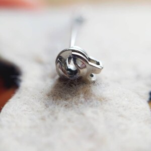 May include: Close-up of a silver safety pin with a coiled spring.