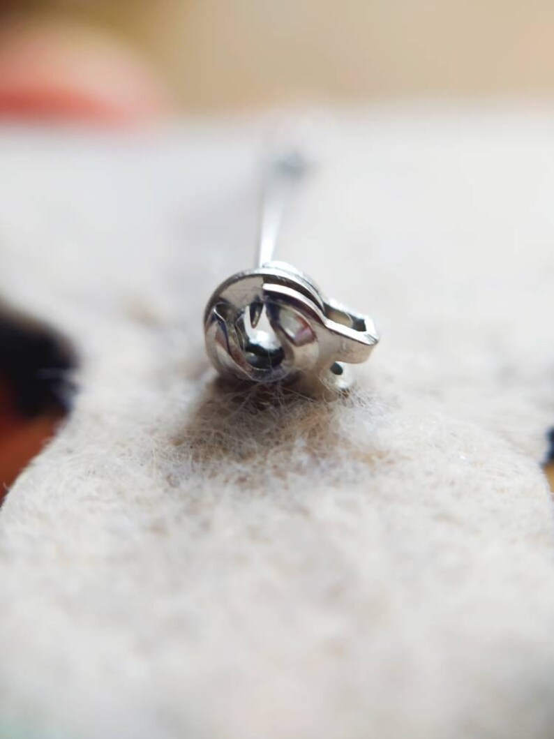 May include: Close-up of a silver safety pin with a coiled spring.