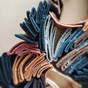 May include: Close-up of a layered paper art piece with a variety of colors, including black, brown, white, and red. The paper is folded and layered to create a three-dimensional effect.