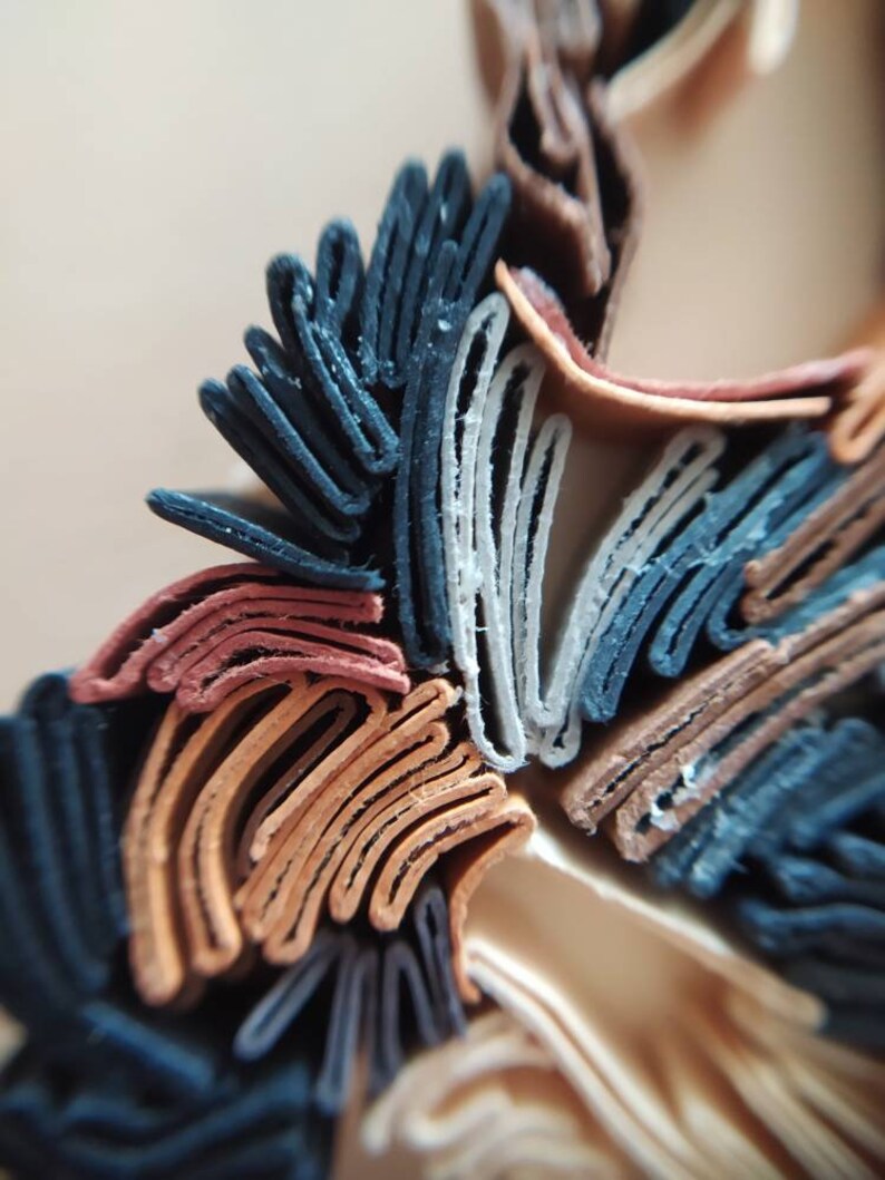 May include: Close-up of a layered paper art piece with a variety of colors, including black, brown, white, and red. The paper is folded and layered to create a three-dimensional effect.