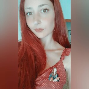 May include: A woman with long, red hair wearing a red dress with white polka dots. She is wearing a pin of the Mona Lisa on her dress.