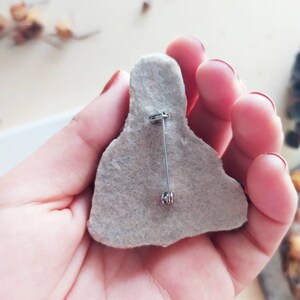 May include: The back of a felt brooch with a silver pin and clasp.