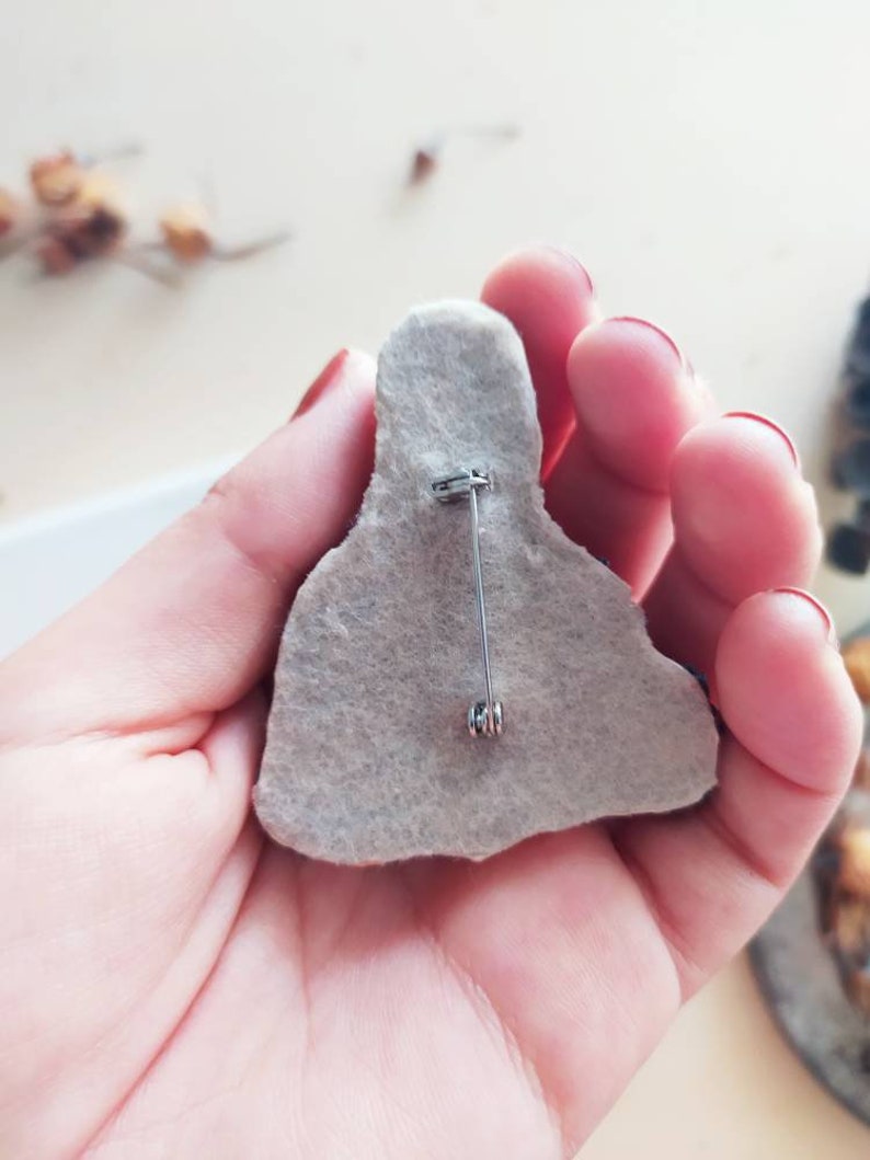 May include: The back of a felt brooch with a silver pin and clasp.