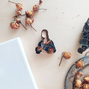 May include: A paper quilling art piece depicting a portrait of the Mona Lisa. The artwork is made of colorful paper strips that are rolled and glued together to create a three-dimensional effect. The artwork is set against a light beige background.