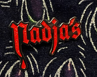 May include: A red glitter enamel pin with the word "Plagjas" in a gothic font.