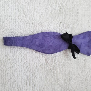 May include: A purple bow tie with a black ribbon. The bow tie has a subtle floral pattern.