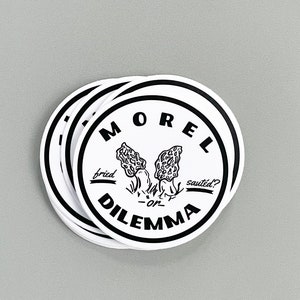 May include: A stack of round white stickers with black text and a black and white illustration of morel mushrooms. The text reads "Morel Dilemma" with "fried" and "saut&eacute;ed?" written below the mushrooms.