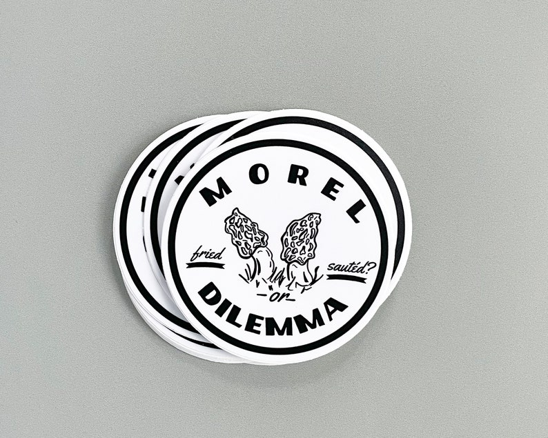 May include: A stack of round white stickers with black text and a black and white illustration of morel mushrooms. The text reads "Morel Dilemma" with "fried" and "saut&eacute;ed?" written below the mushrooms.